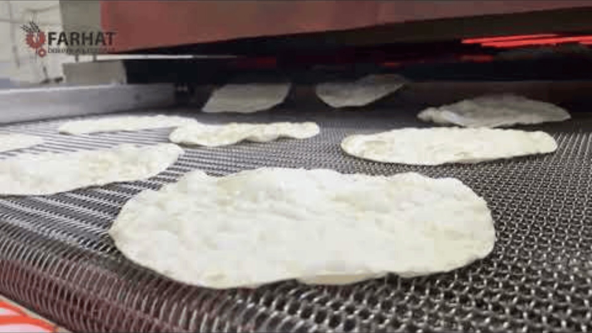 Flatbreads move on a conveyor belt under a heating element in a commercial baking machine. The Farhat logo can be seen in the top left corner of the picture.