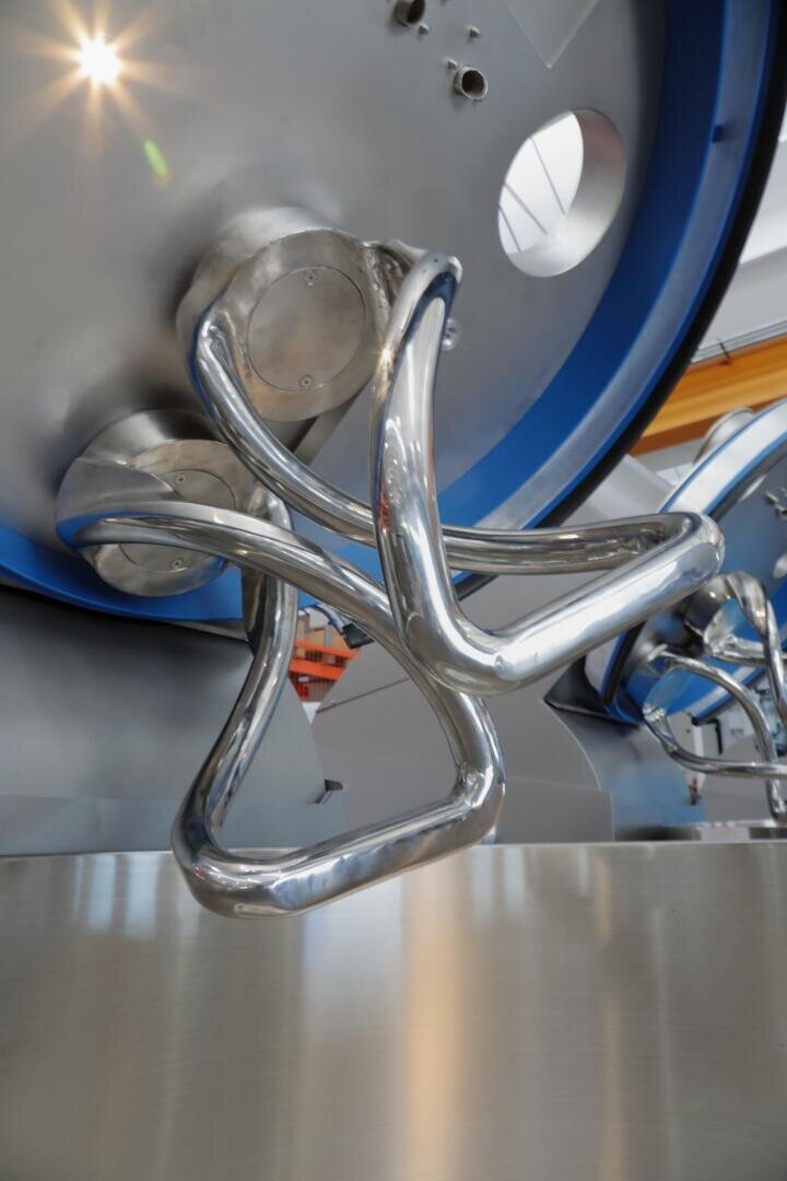 A close-up of a shiny, modern metallic mixing arm inside industrial equipment, with a blue circular border and stainless steel surfaces reflecting light.