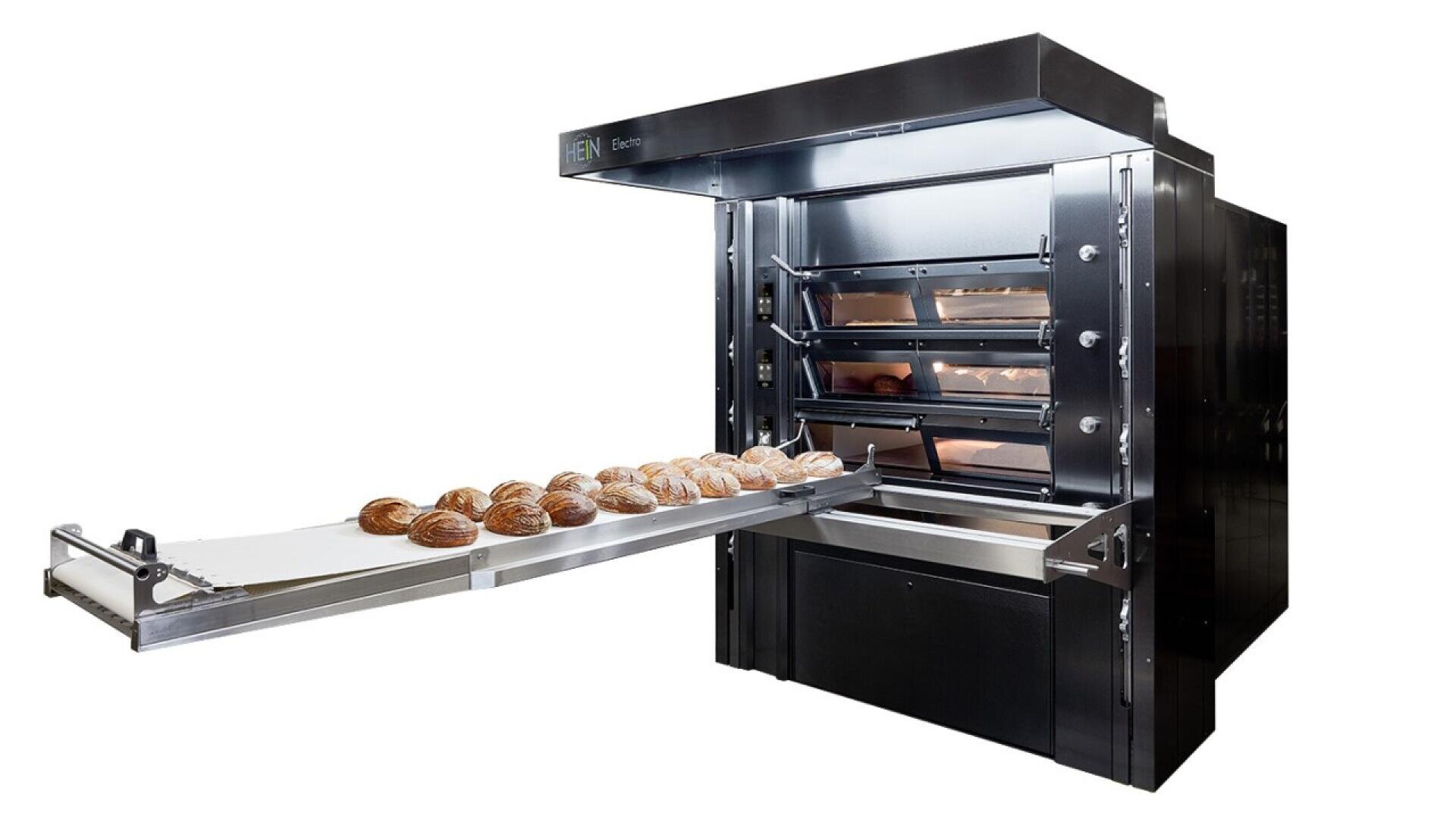 A commercial black baking oven with three shelves, each holding loaves of bread. A conveyor tray is extended from the oven, displaying several round loaves of baked bread.