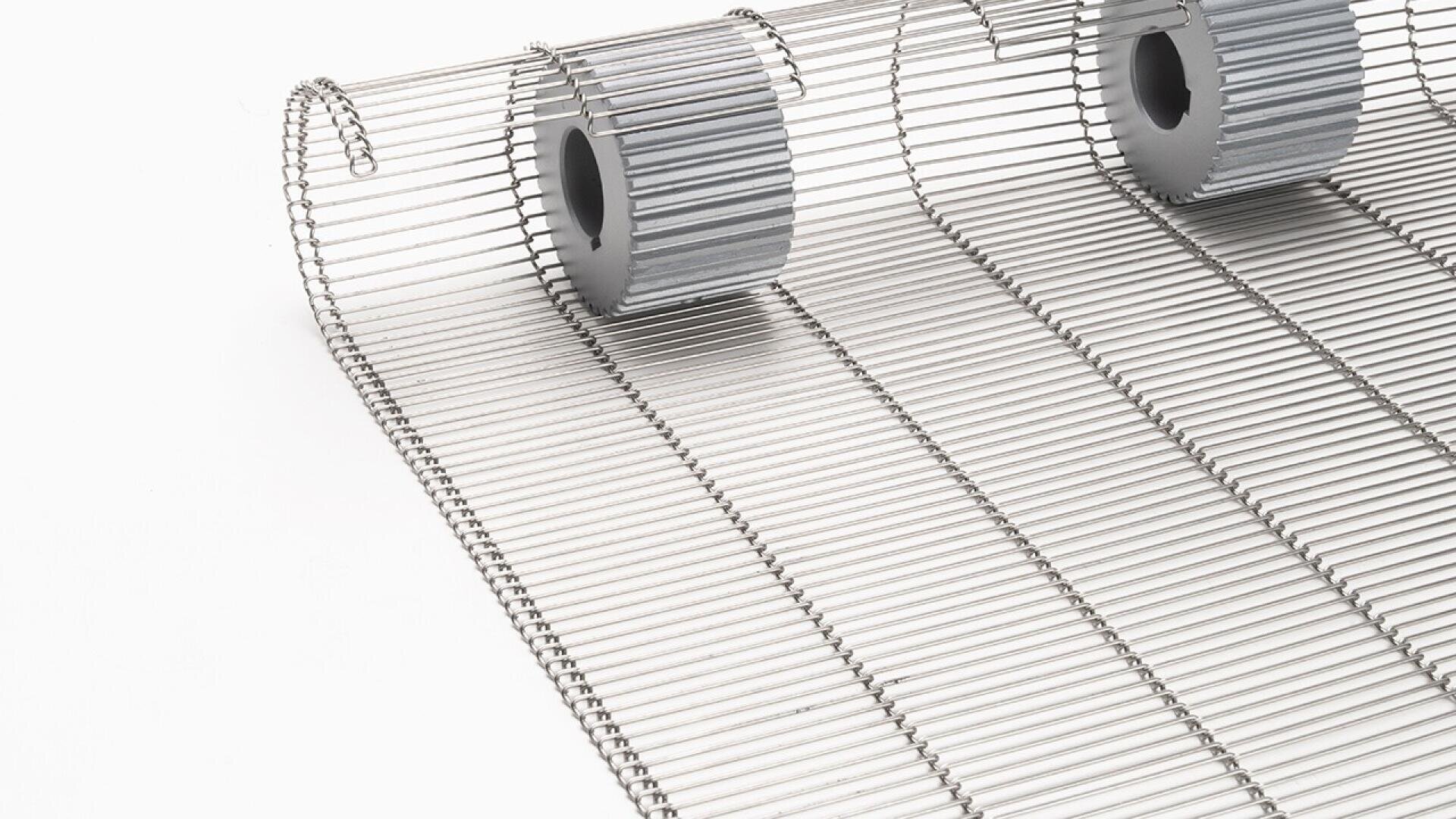 Nahaufnahme eines Metallförderbandes mit gleichmäßig verteilten horizontalen Stangen und zwei darauf positionierten grauen zylindrischen Rollen, fotografiert vor einem weißen Hintergrund.