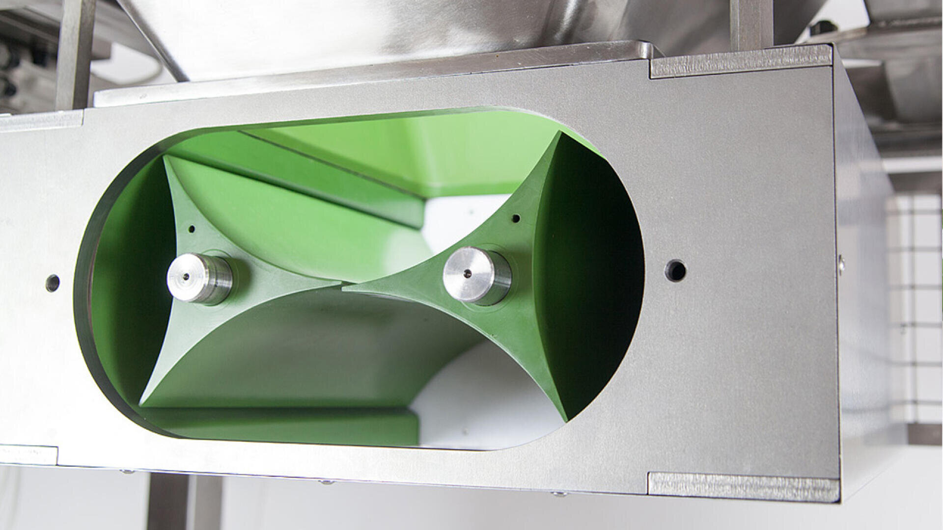 Close-up of a stainless steel industrial machine with a green interior and two cylindrical metal rods, likely part of a mixing, processing, or transport mechanism.