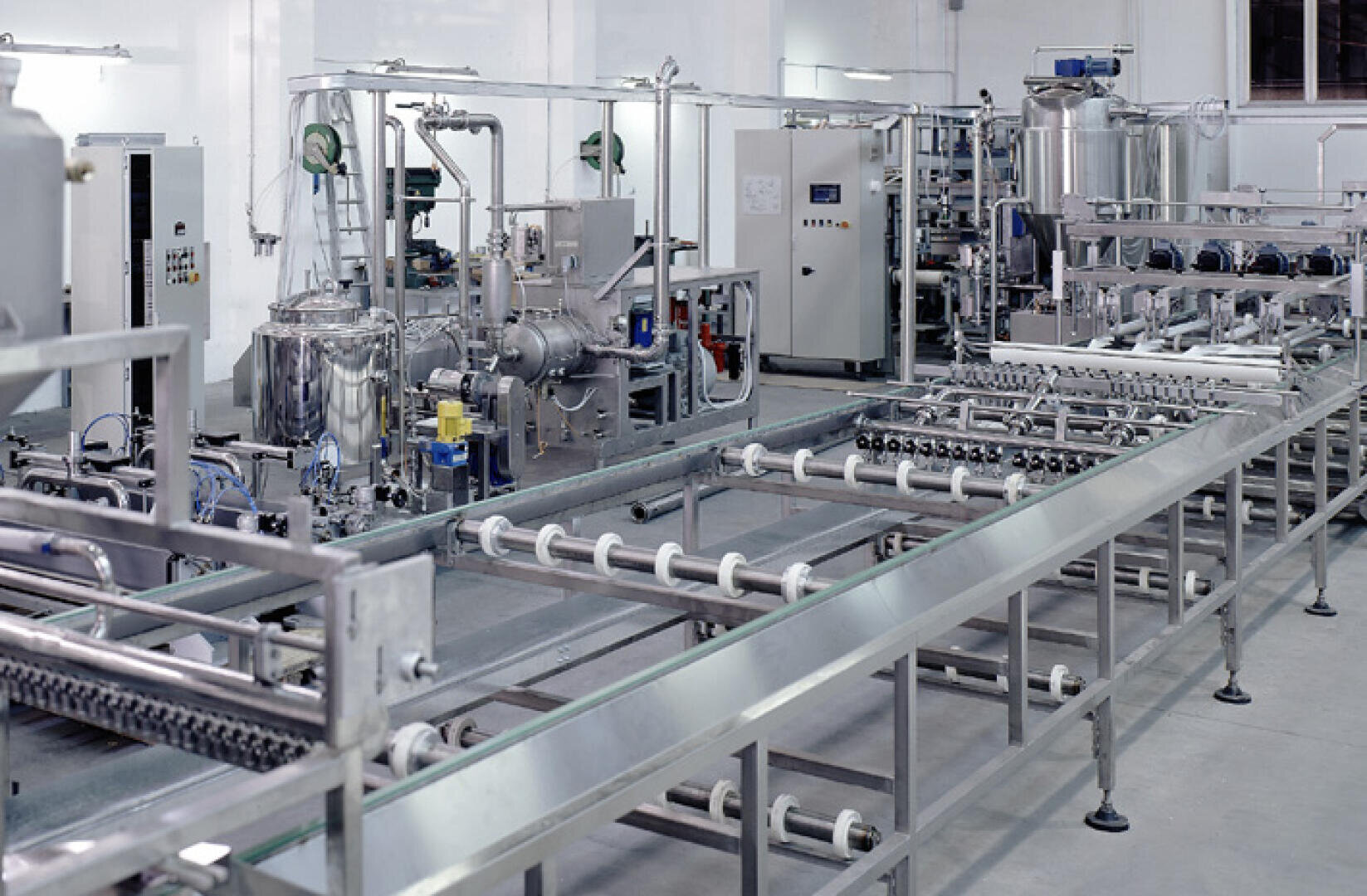 Eine moderne, saubere Lebensmittelverarbeitungs- oder Verpackungsfabrik mit Maschinen, Förderbändern, Tanks und verschiedenen Geräten aus Edelstahl, alles angeordnet in einer gut beleuchteten, organisierten Industrieumgebung.