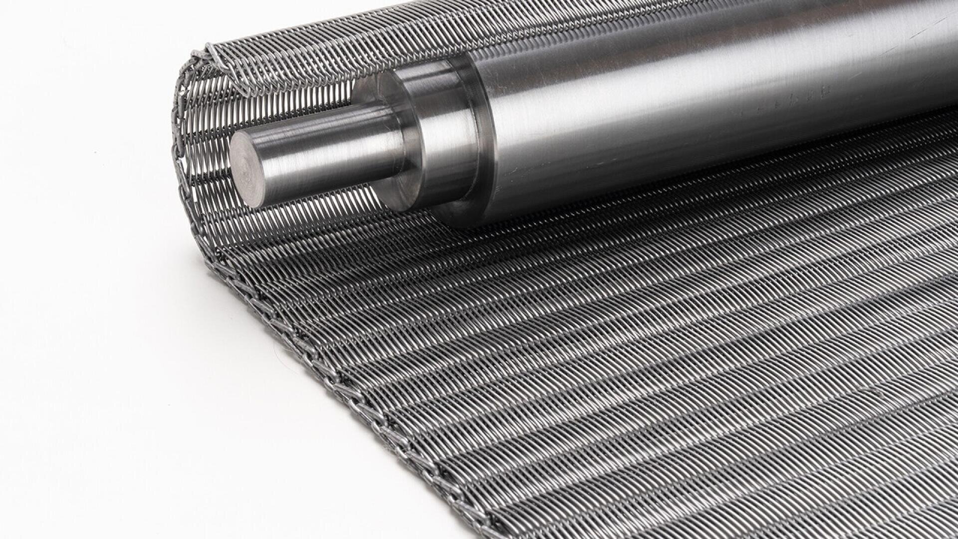 Nahaufnahme einer zylindrischen Metallwalze, die auf einem dicht gewebten Metalldrahtgeflecht ruht. Beide Walzen haben eine glänzende, polierte Oberfläche. Der Hintergrund ist weiß.