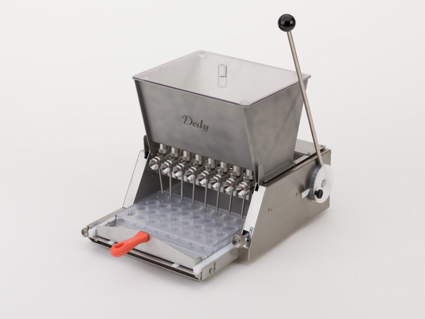 Eine Maschine aus rostfreiem Stahl mit einem Trichter mit der Aufschrift Dedly, Dosierdüsen aus Metall, einem Hebel an der Seite und einem Tablett mit mehreren Formen unter den Düsen.