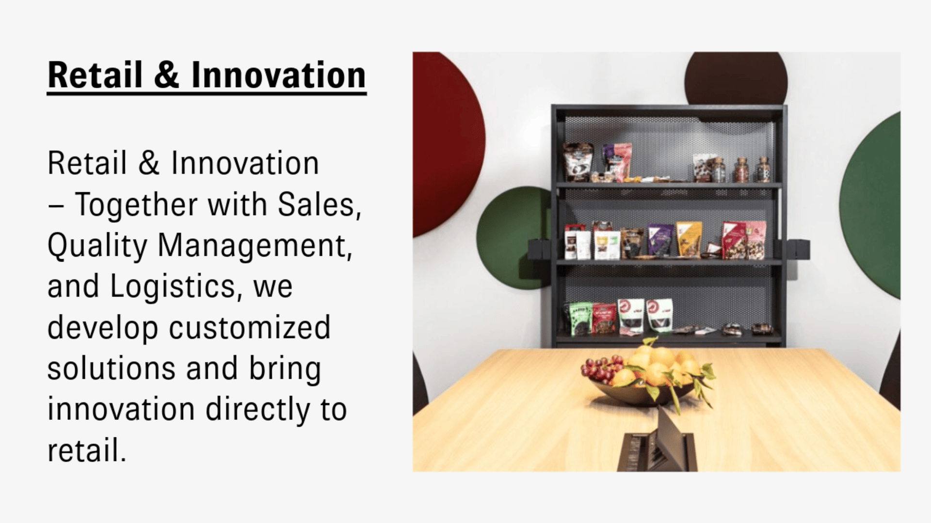 An einer dekorierten weißen Wand steht neben einem Holztisch mit Obst ein Regal mit verschiedenen Snacks und Produkten. In Fettdruck steht „Einzelhandel und Innovation“ mit einer Beschreibung maßgeschneiderter Einzelhandelslösungen.
