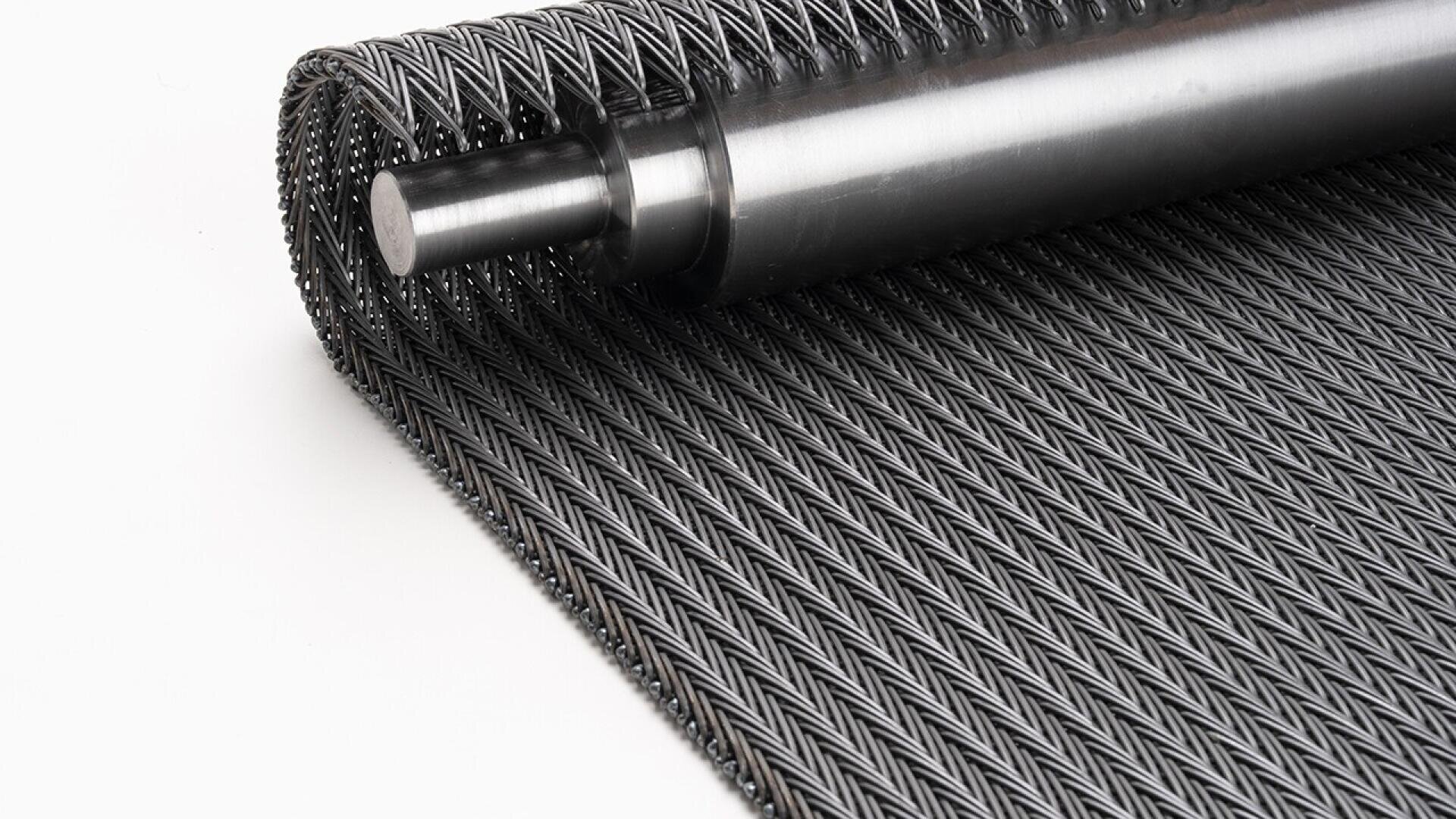 Eine Nahaufnahme eines aufgerollten Metallförderbandes mit einer zylindrischen Metallstange, die das verwobene Stahlgittermuster auf einem schlichten weißen Hintergrund zeigt.