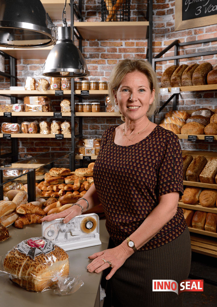 A woman stands in a bakery with shelves of bread behind her, smiling and using an Inno Seal machine to seal a packaged loaf of bread on the counter. The Inno Seal logo appears in the bottom right corner.