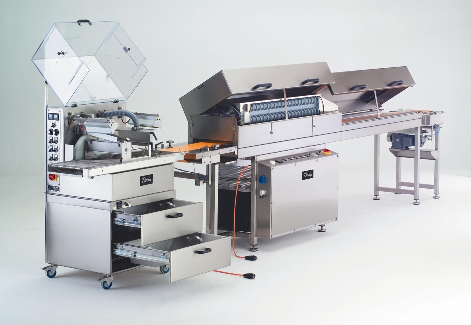 Eine große industrielle Lebensmittelverarbeitungsmaschine aus rostfreiem Stahl mit mehreren Förderbändern, offenen Fächern, Schalttafeln und Ablagefächern vor einem schlichten weißen Hintergrund.