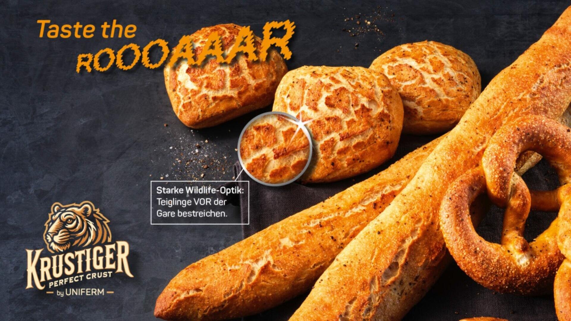 Various loaves and rolls of tiger bread with a distinctive cracked crust are displayed on a dark surface. Taste the ROOOOOAR and the Krustiger logo with a tiger are shown, highlighting the bread’s texture.