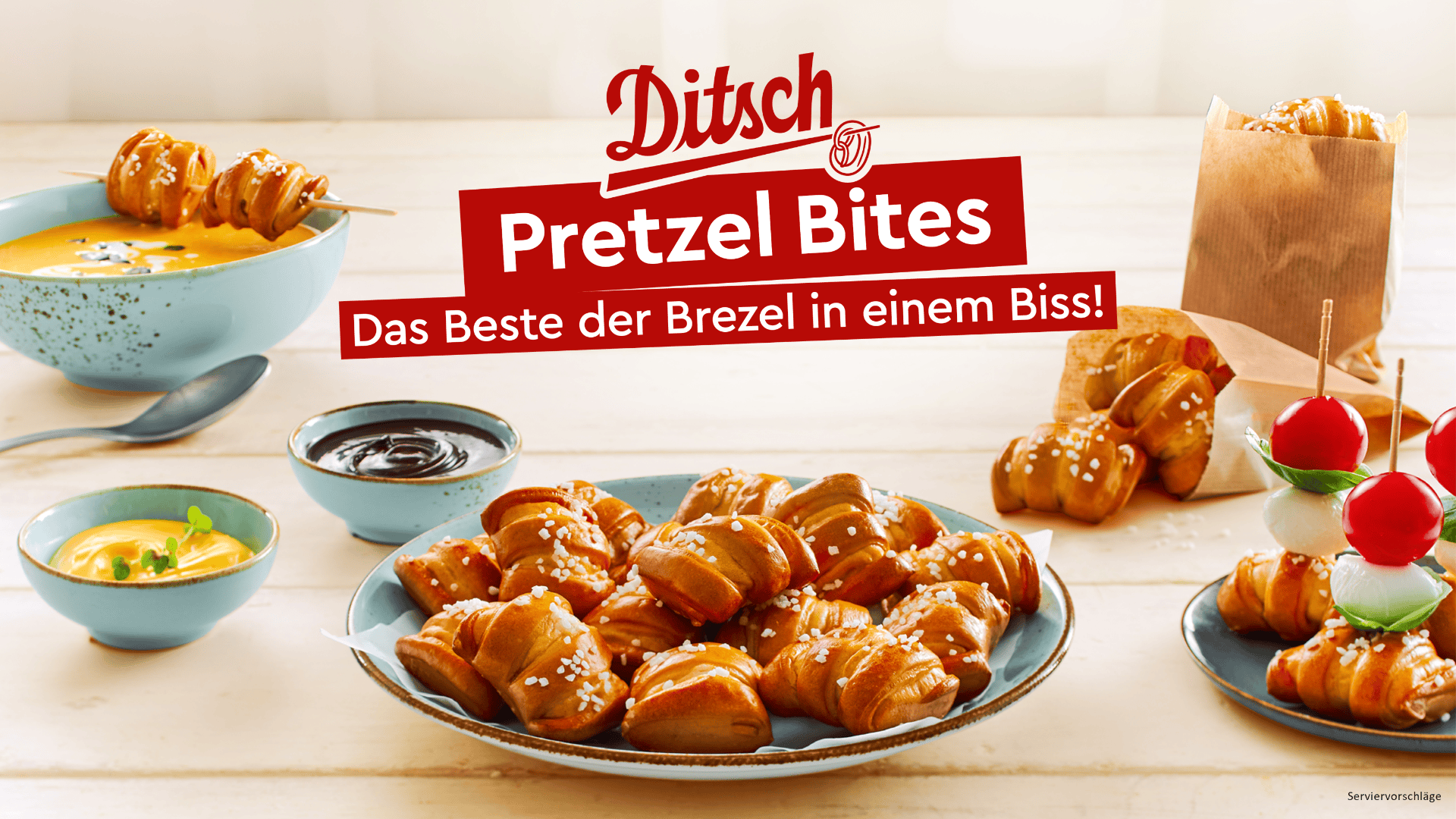 Verschiedene Brezelbissen auf Tellern mit Dip-Saucen, eine Schüssel Suppe und Spieße mit Käse, Tomaten und Brezelbissen. Eine Papiertüte mit Laugengebäck steht im Hintergrund. Der rote Schriftzug Ditsch Pretzel Bites steht oben.