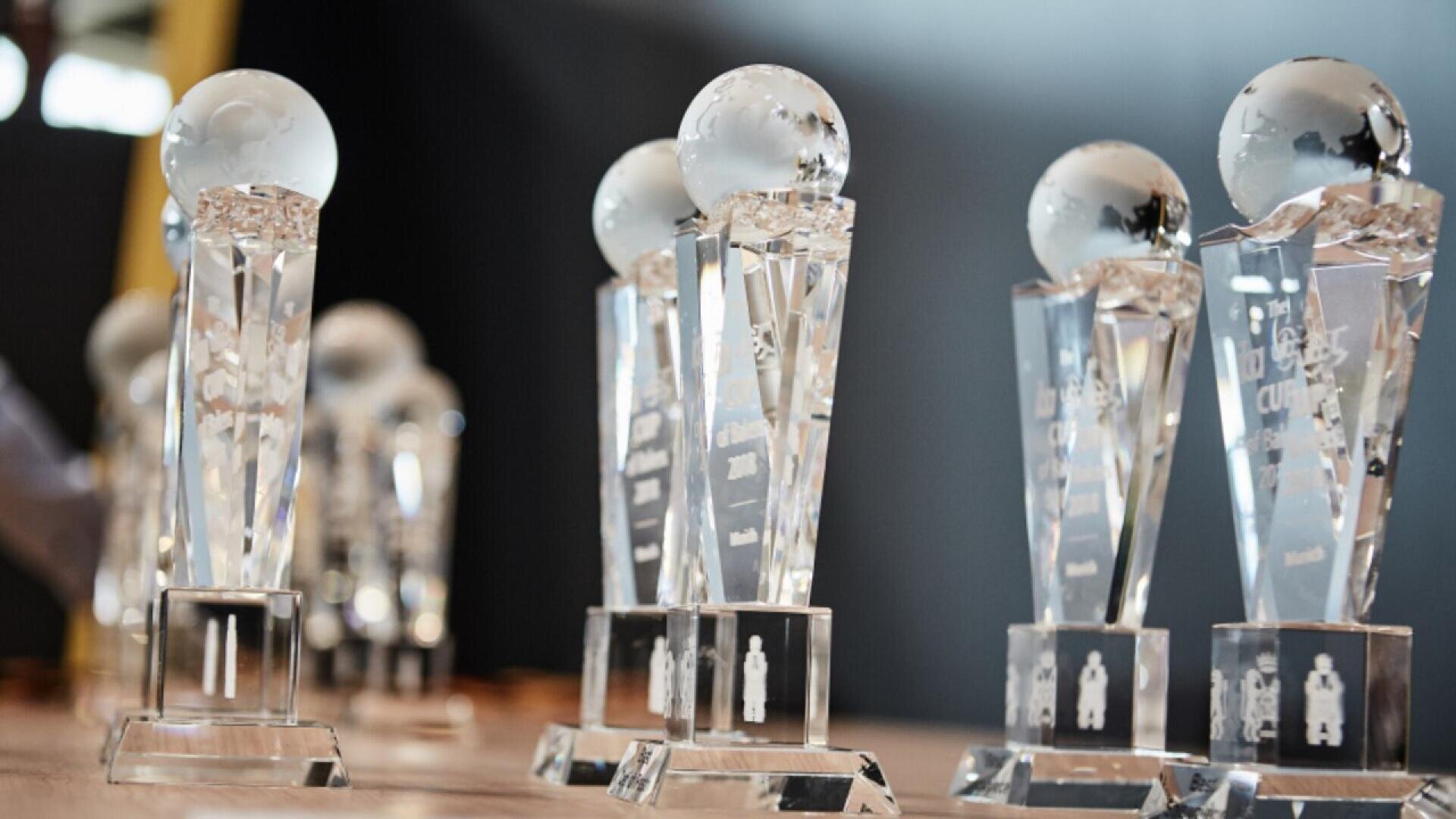 Several crystal trophies with globe-shaped tops are displayed on a table, ready for an awards event. The trophies have a faceted, clear design and are engraved with text and figures.