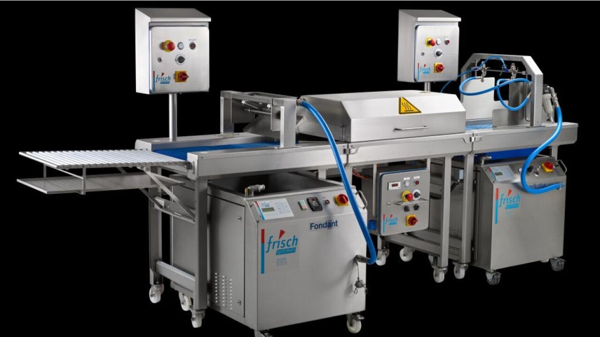 Industrial bakery machine with conveyor belts, control panels, blue hoses, and stainless steel components, designed for automated pastry production, set against a black background.