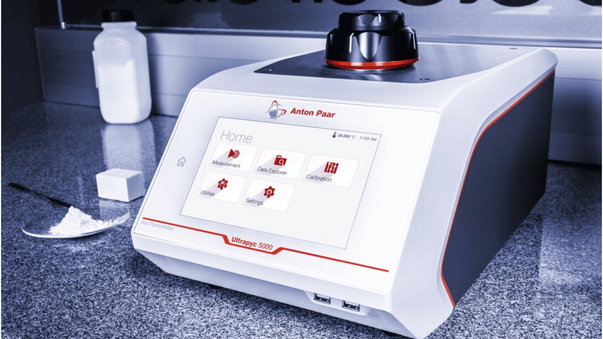 Ein Labortischgerät, das Anton Paar Ultrapyc 5000, steht auf einer Arbeitsplatte. Ein Touchscreen-Display zeigt Menüoptionen an. Pulver und ein Spatel liegen daneben, im Hintergrund steht ein weißer Behälter.