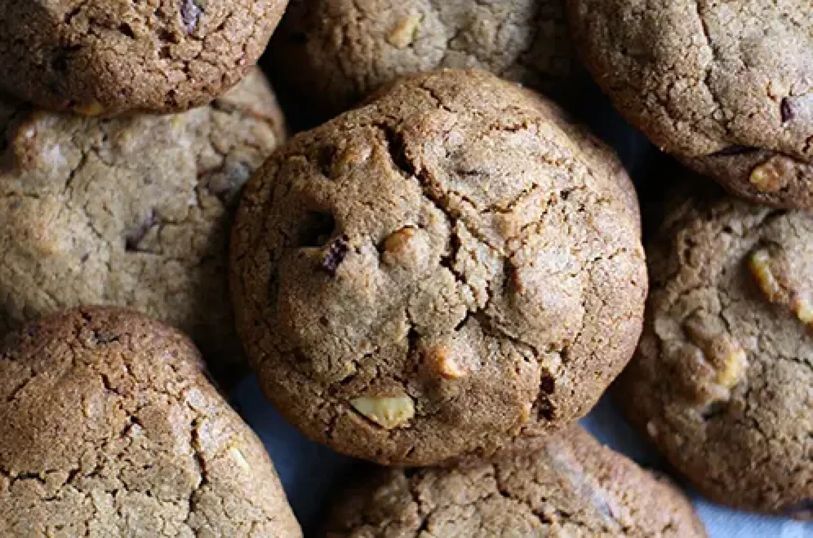 A close-up view of several golden-brown cookies with a cracked surface, showcasing visible pieces of nuts and chocolate chips.