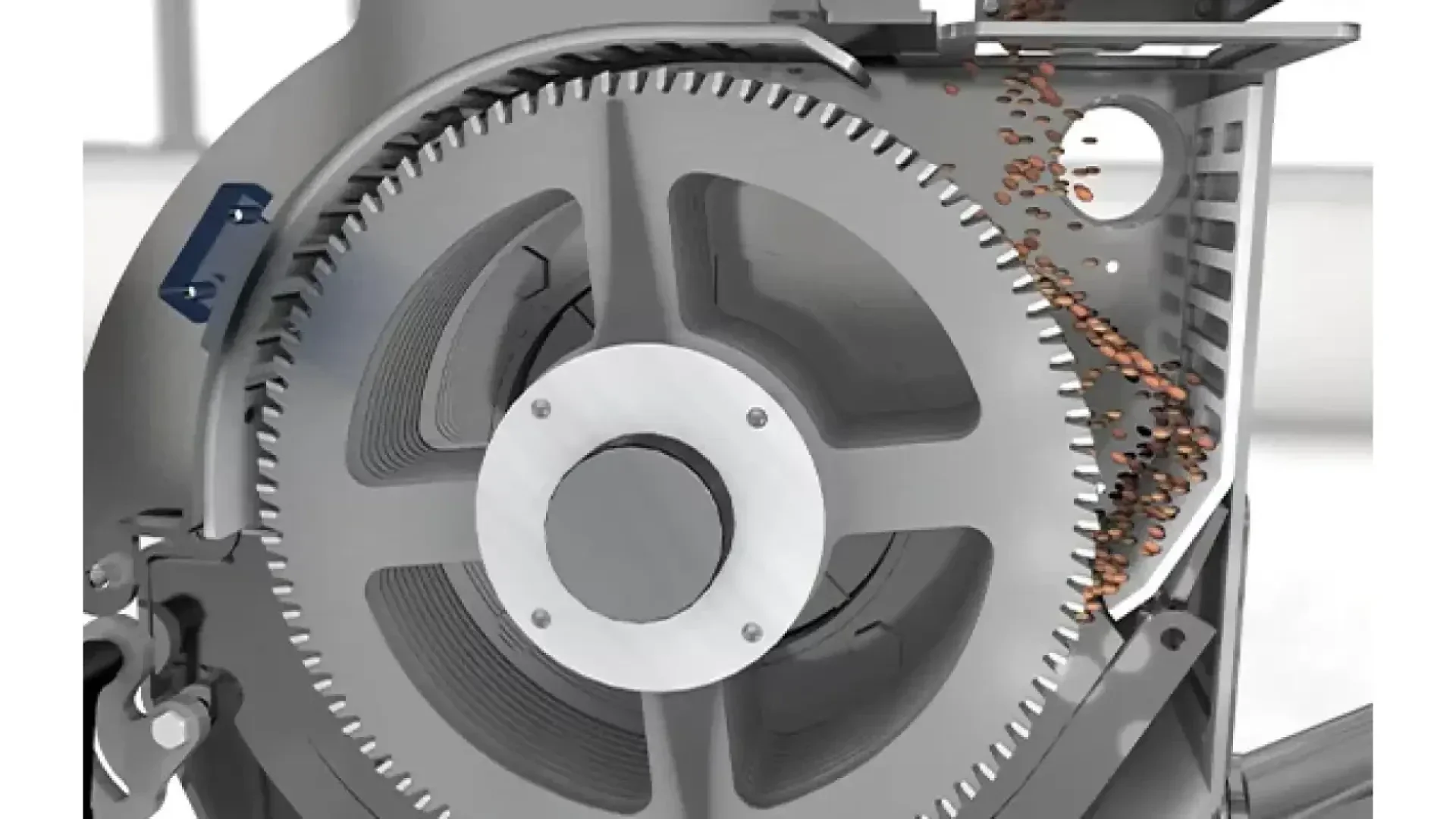 Close-up of a large industrial gear mechanism with small brown pellets or particles being processed and moved along the side inside a metal machine.