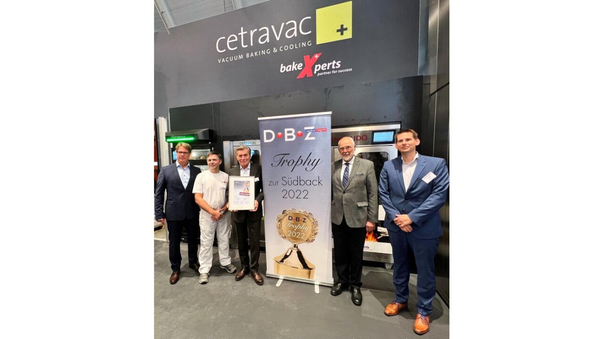 Five men stand in front of a display with “cetravac” and “bakeXperts” signage. They are holding a framed certificate and a banner reads “DBZ Trophy zur Südback 2022.” All are dressed in business or professional attire.
