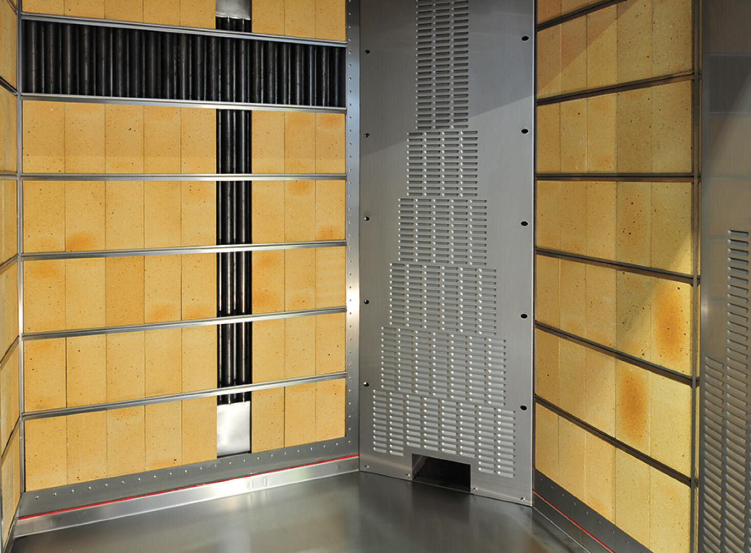 Ein modernes industrielles Ofeninnere mit metallischen und isolierten gelben Paneelen an den Wänden, belüfteten Bereichen und einem sauberen, reflektierenden Stahlboden.