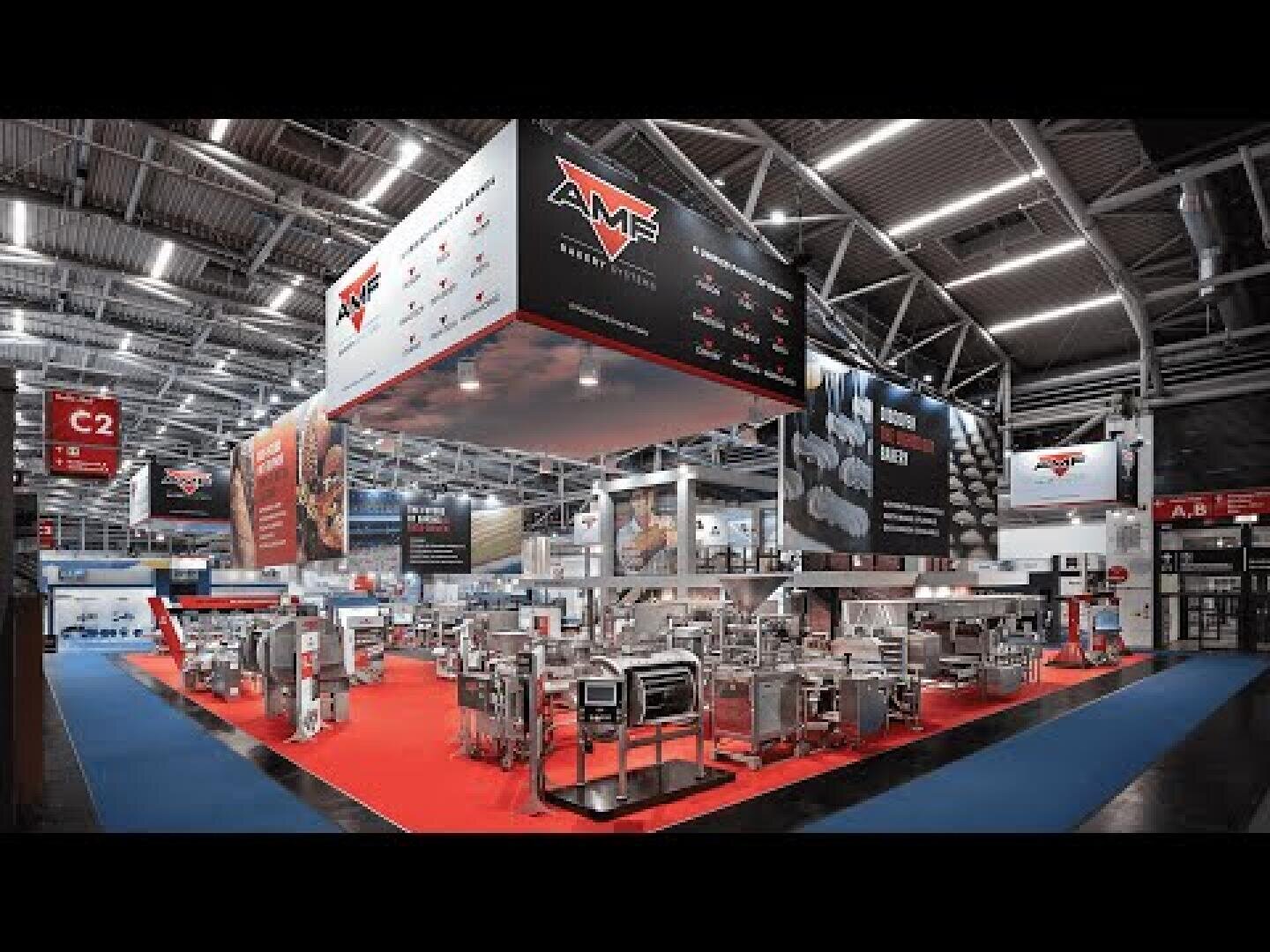 A large exhibition booth displays industrial food processing equipment on a red carpet. Overhead signs show the AMF logo. The venue has bright lighting and high ceilings, with various machines arranged neatly.