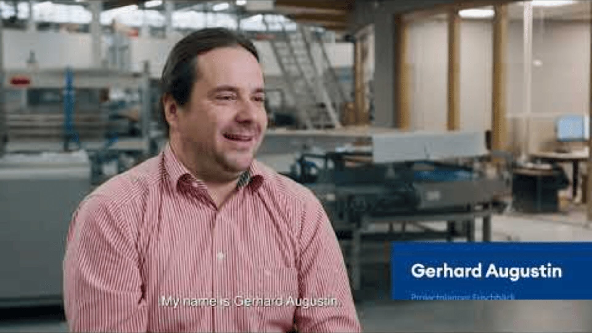 A man in a red striped shirt sits smiling in a modern industrial workspace. A caption reads, My name is Gerhard Augustin. A blue label on the right displays Gerhard Augustin and his job title.