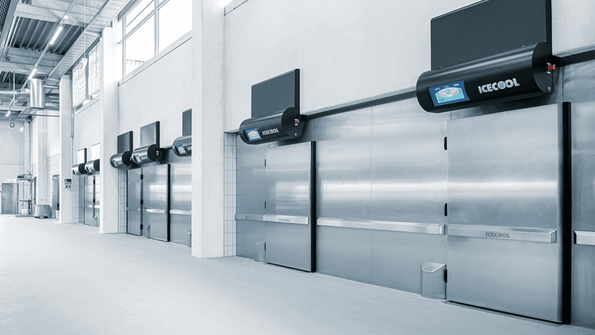 Eine Reihe industrieller Kühlhaustüren aus Edelstahl mit darüber montierten elektronischen Schalttafeln in einer sauberen, modernen Kühlhausanlage.