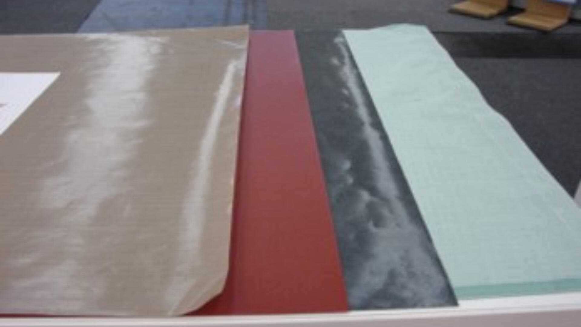 Vier Blätter aus verschiedenfarbigen und unterschiedlich strukturierten Materialien - beige, rot, schwarz und hellblau - werden nebeneinander auf einer ebenen Fläche ausgelegt.