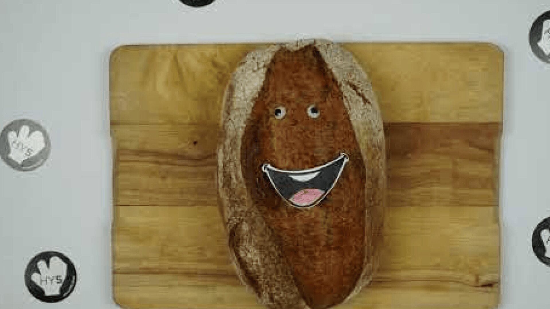 Ein Laib Brot auf einem hölzernen Schneidebrett mit Cartoon-Augen und einem lächelnden Mund, die ihm ein fröhliches Gesicht verleihen.