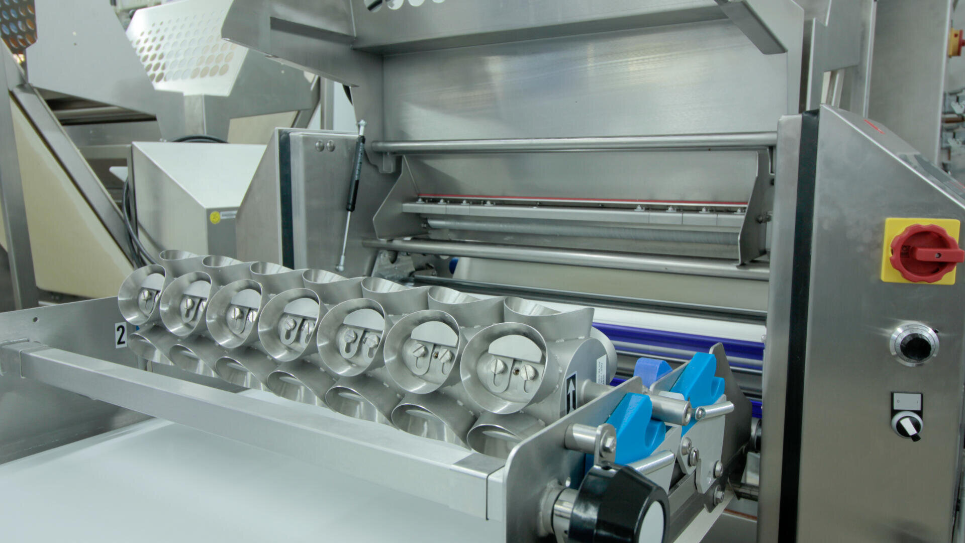 Nahaufnahme einer industriellen Lebensmittelverarbeitungsmaschine aus Edelstahl mit zylindrischen Formen und verschiedenen mechanischen Teilen, die für die automatisierte Produktion in einer Fabrik konzipiert ist.