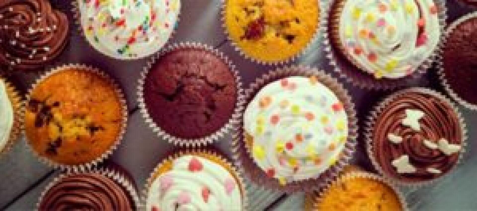 An assortment of cupcakes with colorful sprinkles and swirled frosting, arranged closely together on a light wooden surface.