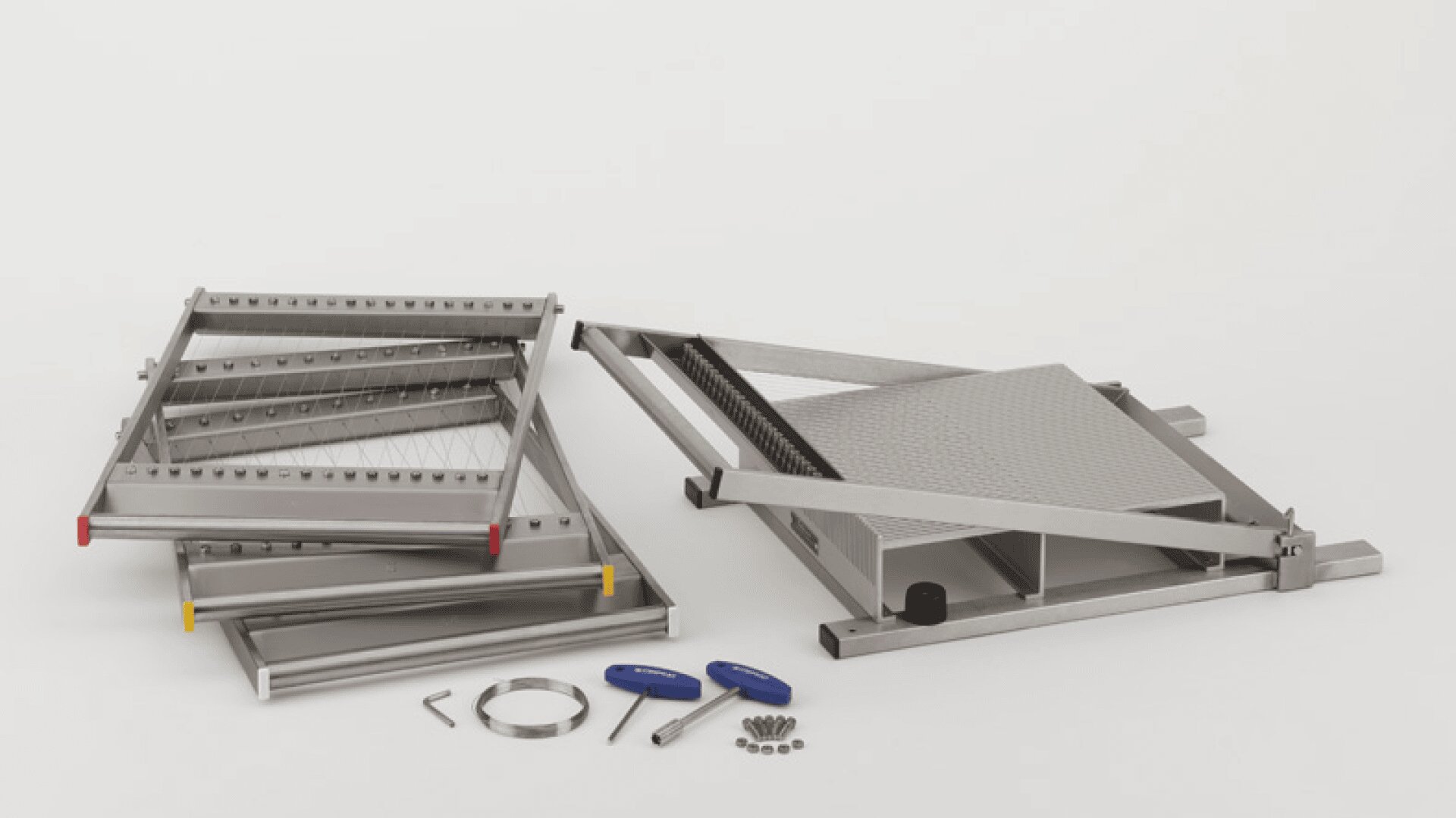 Zerlegtes Metallgerät mit mehreren rechteckigen Bauteilen, Schrauben, zwei Werkzeugen mit blauem Griff, einem Sechskantschlüssel und einem Metallband, alles auf einer weißen Fläche ausgelegt.