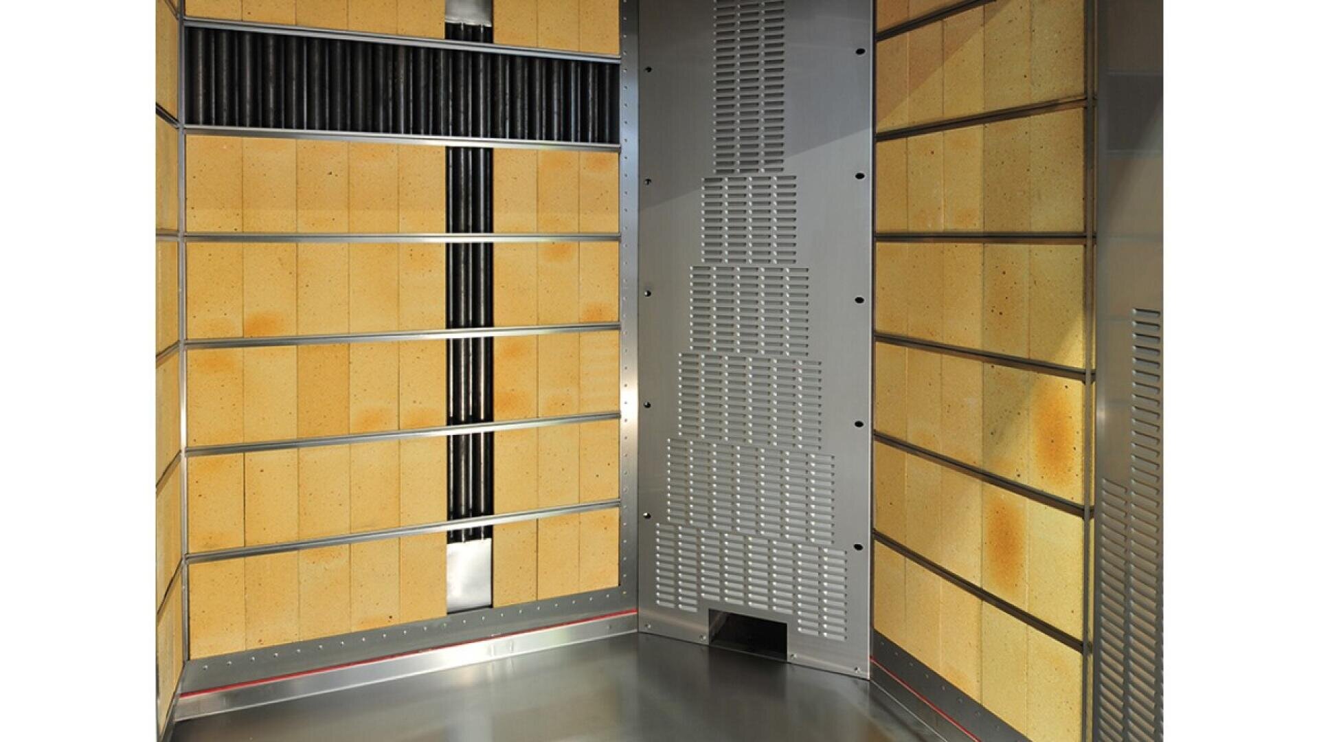 A modern, empty elevator interior with beige wall panels, metallic accents, and a stainless steel floor. The walls have grid-like patterns and some ventilation or speaker panels.