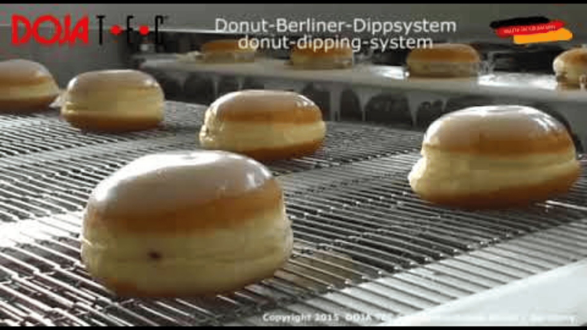Glazed donuts move along a conveyor belt in an automated donut-dipping system at a bakery. Text on the image reads Donut-Berliner-Dippsystem donut-dipping-system.