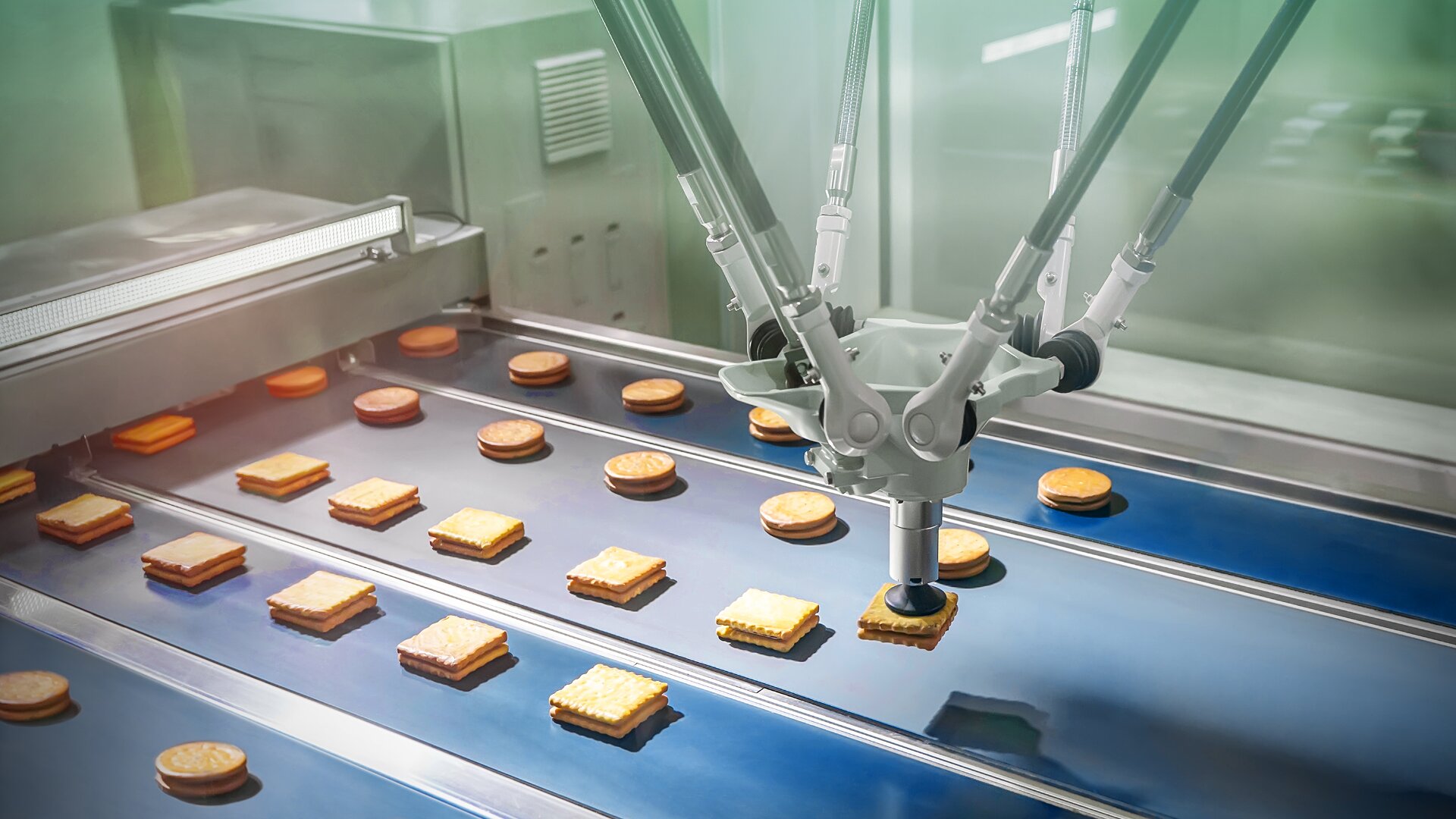 A robotic arm sorts square sandwich cookies on a conveyor belt in a factory, demonstrating automated food production.