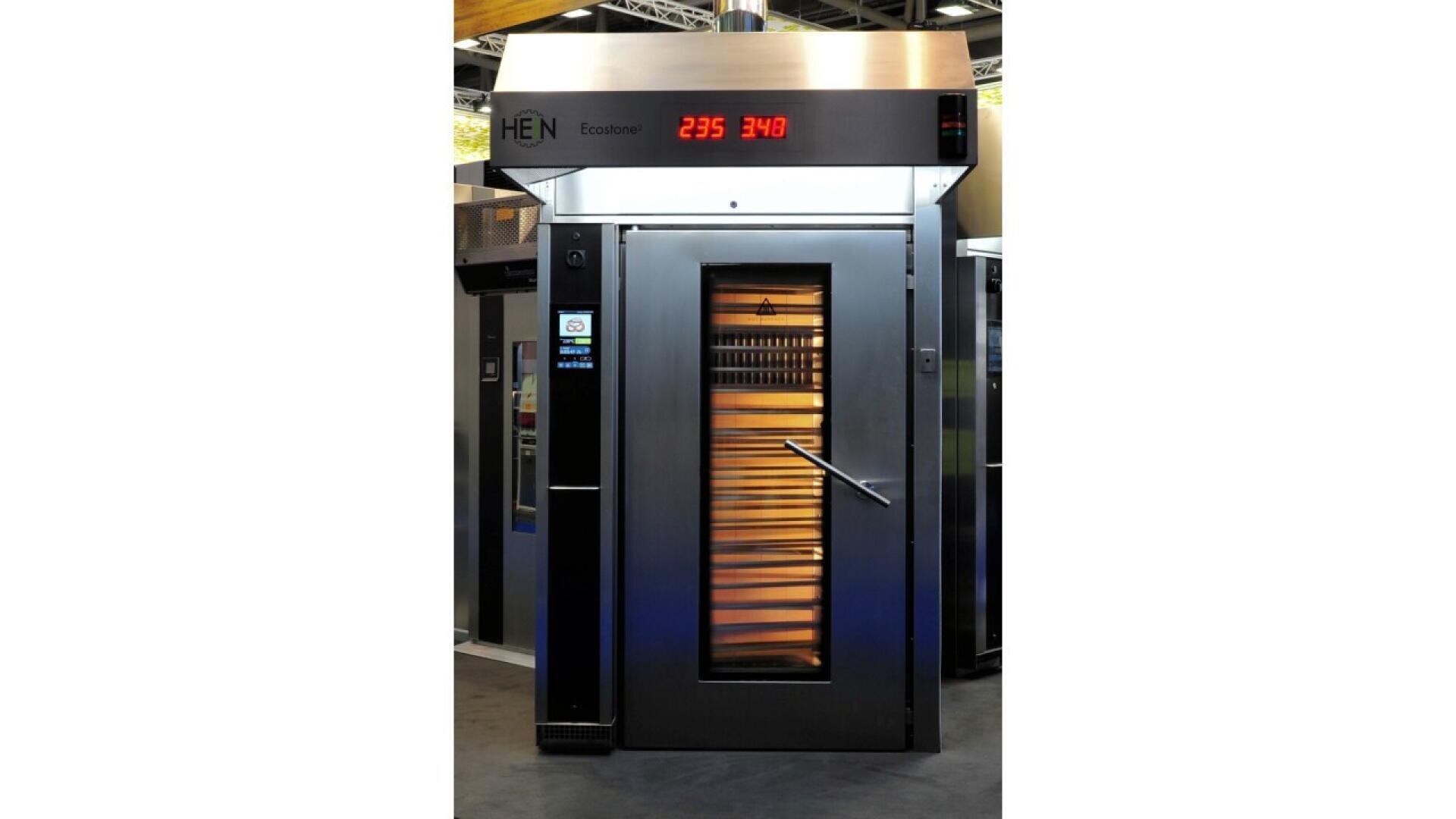 A large commercial oven with a glass door showing trays of baked goods inside. The digital display above reads 235 and 340. The oven is metallic with a handle and control panel on the side.