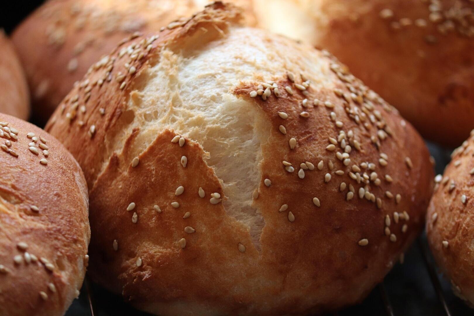 Close-up of freshly baked golden brown bread rolls topped with sesame seeds, showing a crisp crust and soft, fluffy interior.