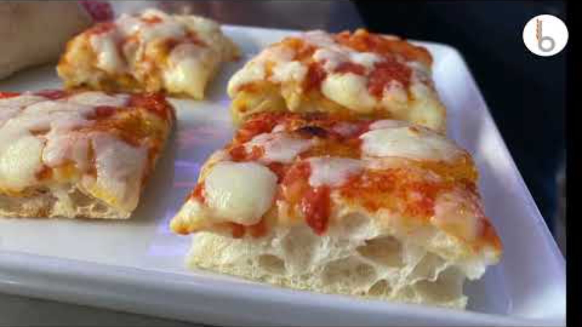 Four square slices of thick, airy focaccia-style pizza with melted cheese and tomato sauce are arranged on a white rectangular plate.