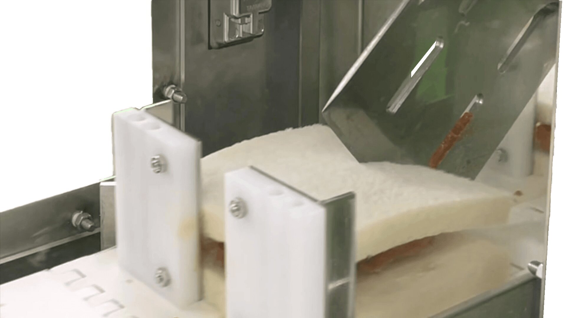Eine Nahaufnahme einer Maschine, die ein Weißbrot in Scheiben schneidet. Das Sandwich wird von zwei weißen Kunststoffführungen gehalten, während eine Metallklinge das Brot durchschneidet.