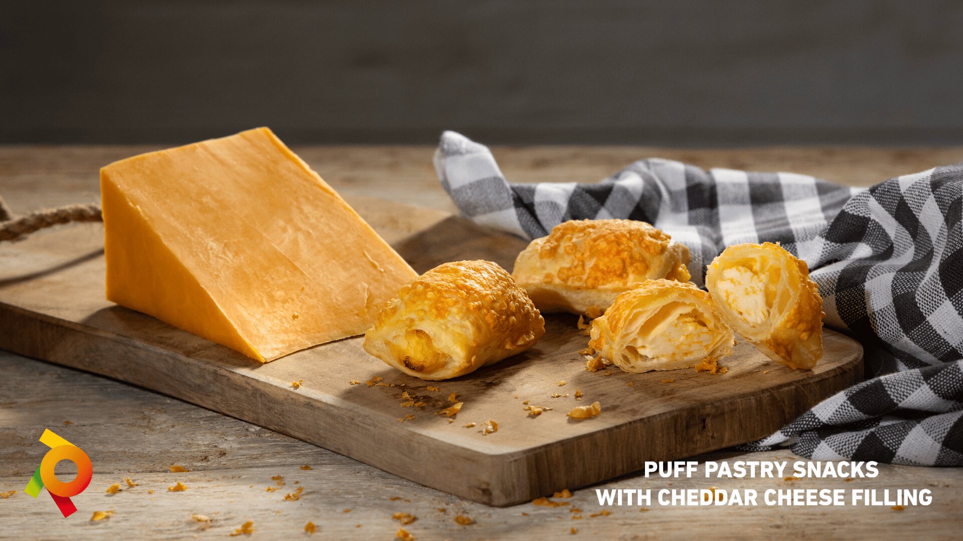 A block of cheddar cheese and three puff pastry snacks with cheddar cheese filling are displayed on a wooden board. A checkered cloth is in the background, and text reads Puff Pastry Snacks With Cheddar Cheese Filling.