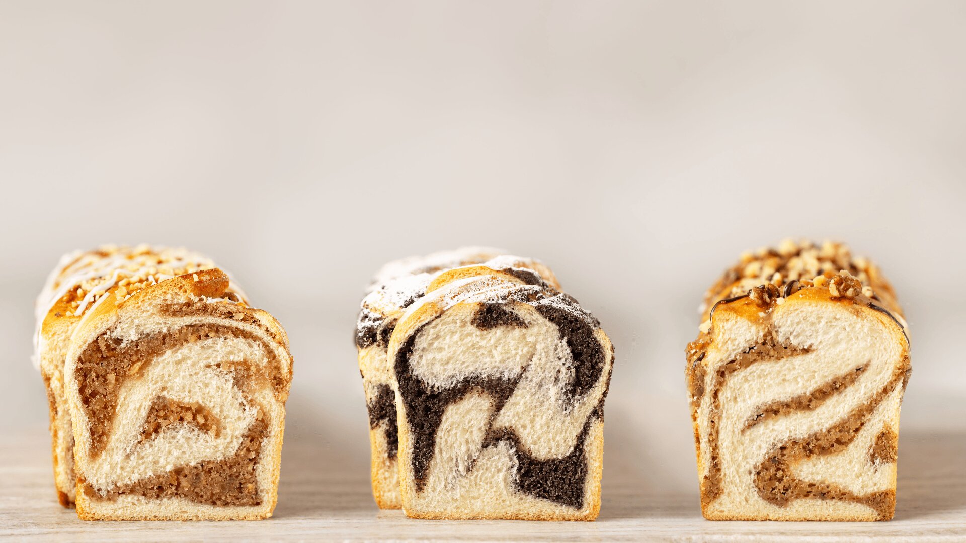 Auf einer hellen Fläche mit neutralem Hintergrund sind drei aufgeschnittene Brote mit unterschiedlichen Belägen in einer Reihe angeordnet.