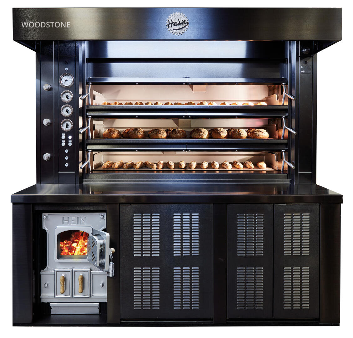 Ein großer kommerzieller Brotofen mit mehreren Einschüben zum Backen von Broten. Der Ofen verfügt über Messgeräte auf der linken Seite, eine Glastür mit Feuer in einem unteren Fach und ein Hein-Logo auf der Oberseite.