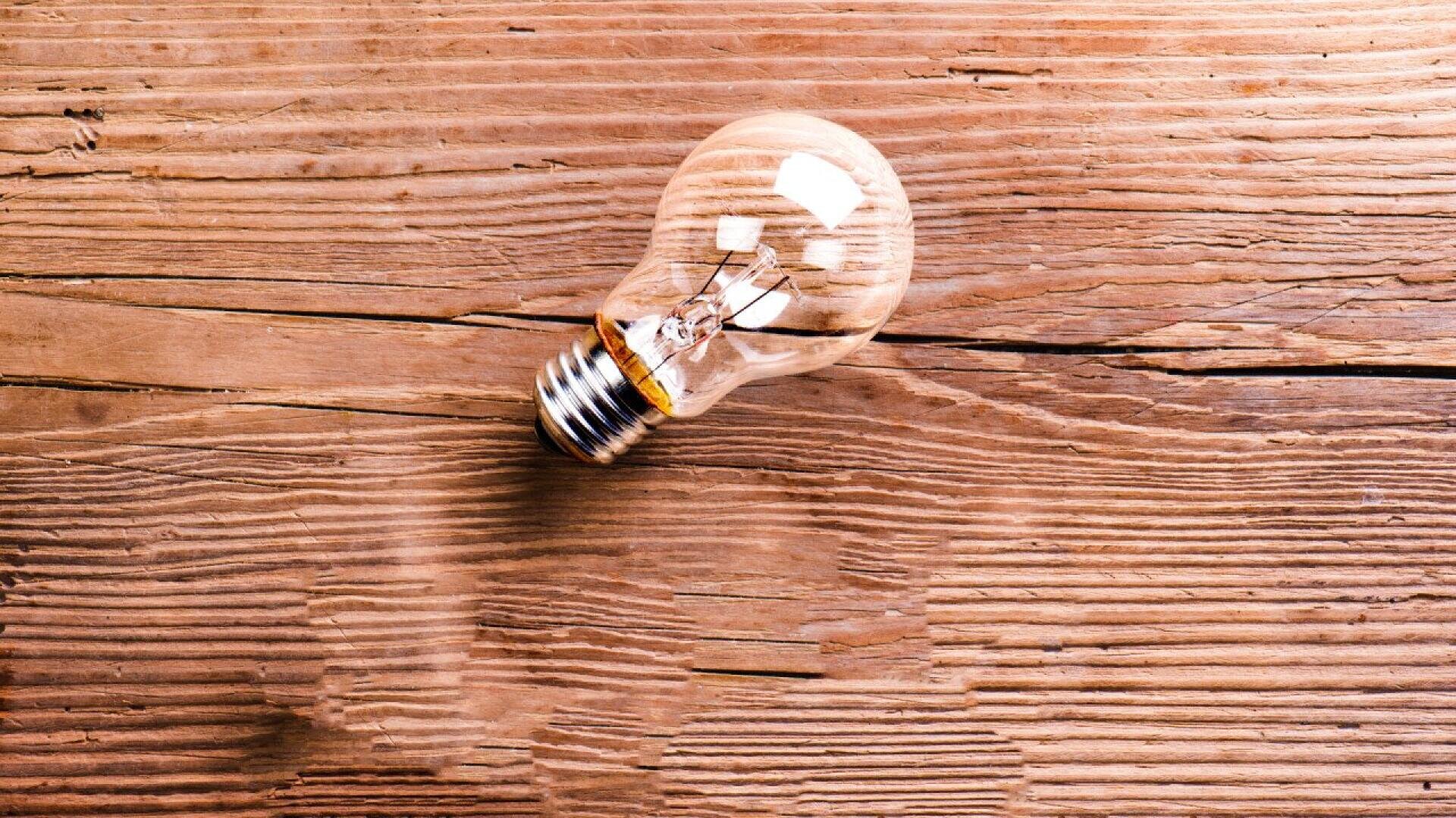 A clear incandescent light bulb lying on its side on a wooden surface with visible grain and texture.