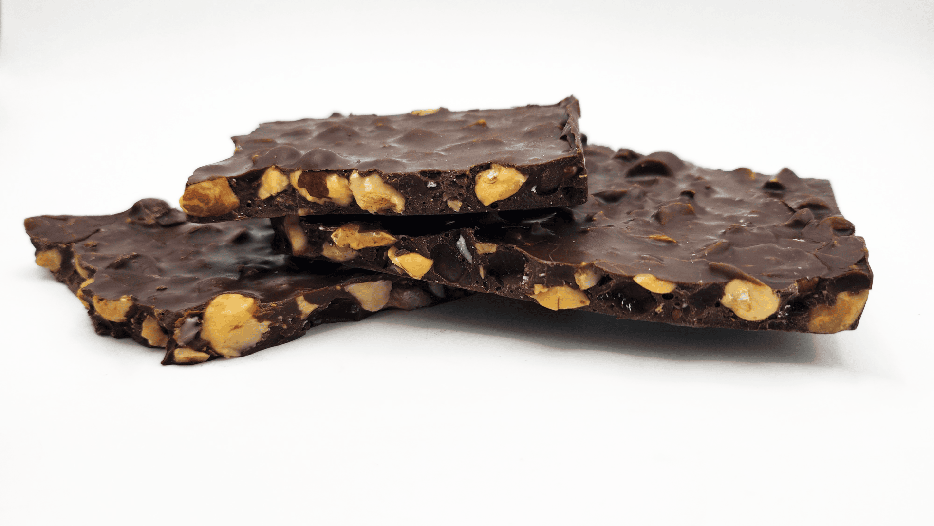 Drei Stücke Schokoladenrinde mit sichtbaren ganzen und gehackten Nüssen, gestapelt auf einem weißen Hintergrund.