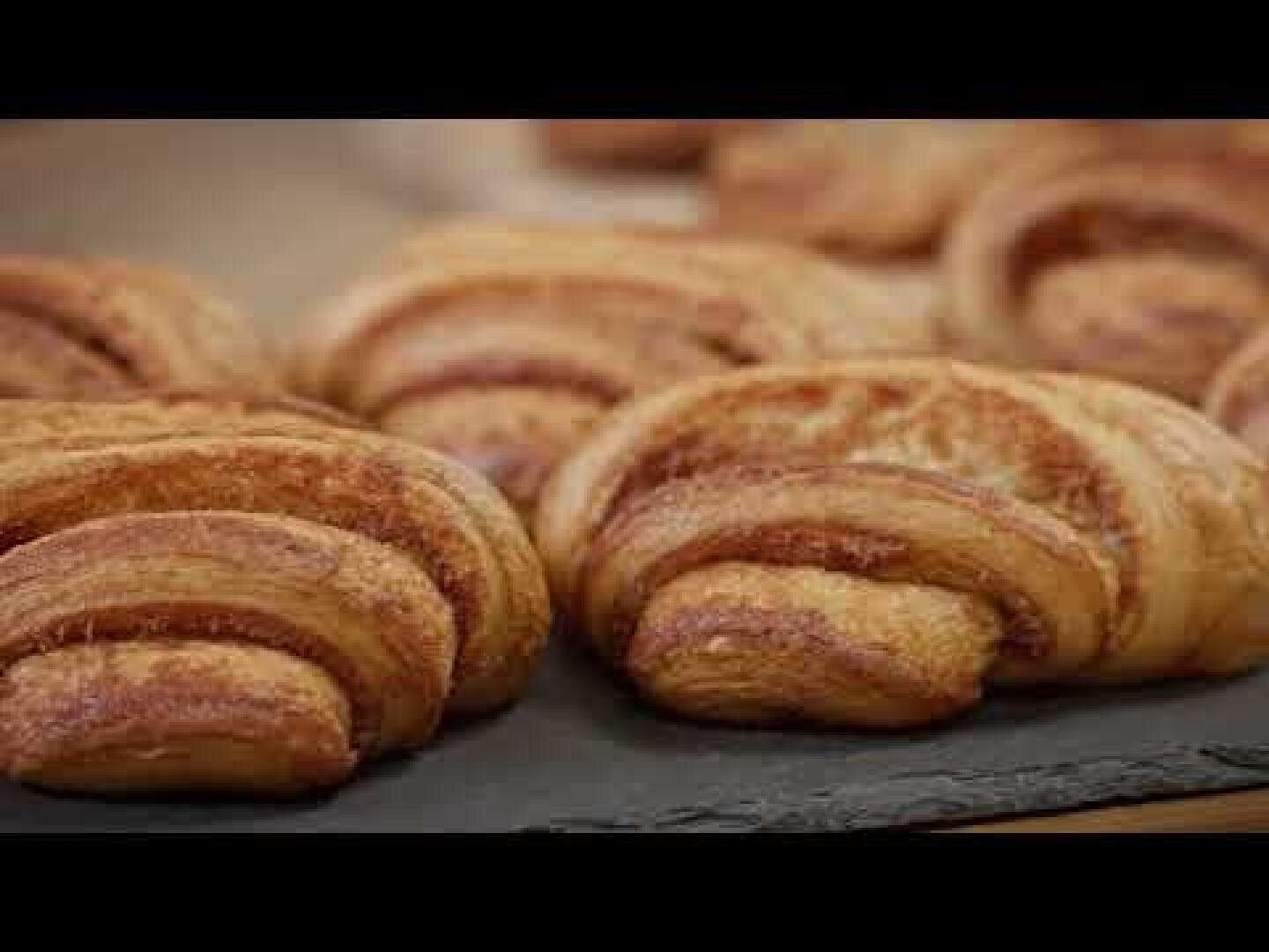 Eine Nahaufnahme von mehreren goldbraunen, flockigen Gebäckstücken, die auf einer dunklen Schieferoberfläche angeordnet sind. Das Gebäck hat ein gewölbtes, geschichtetes Aussehen und eine leicht knusprige Textur.