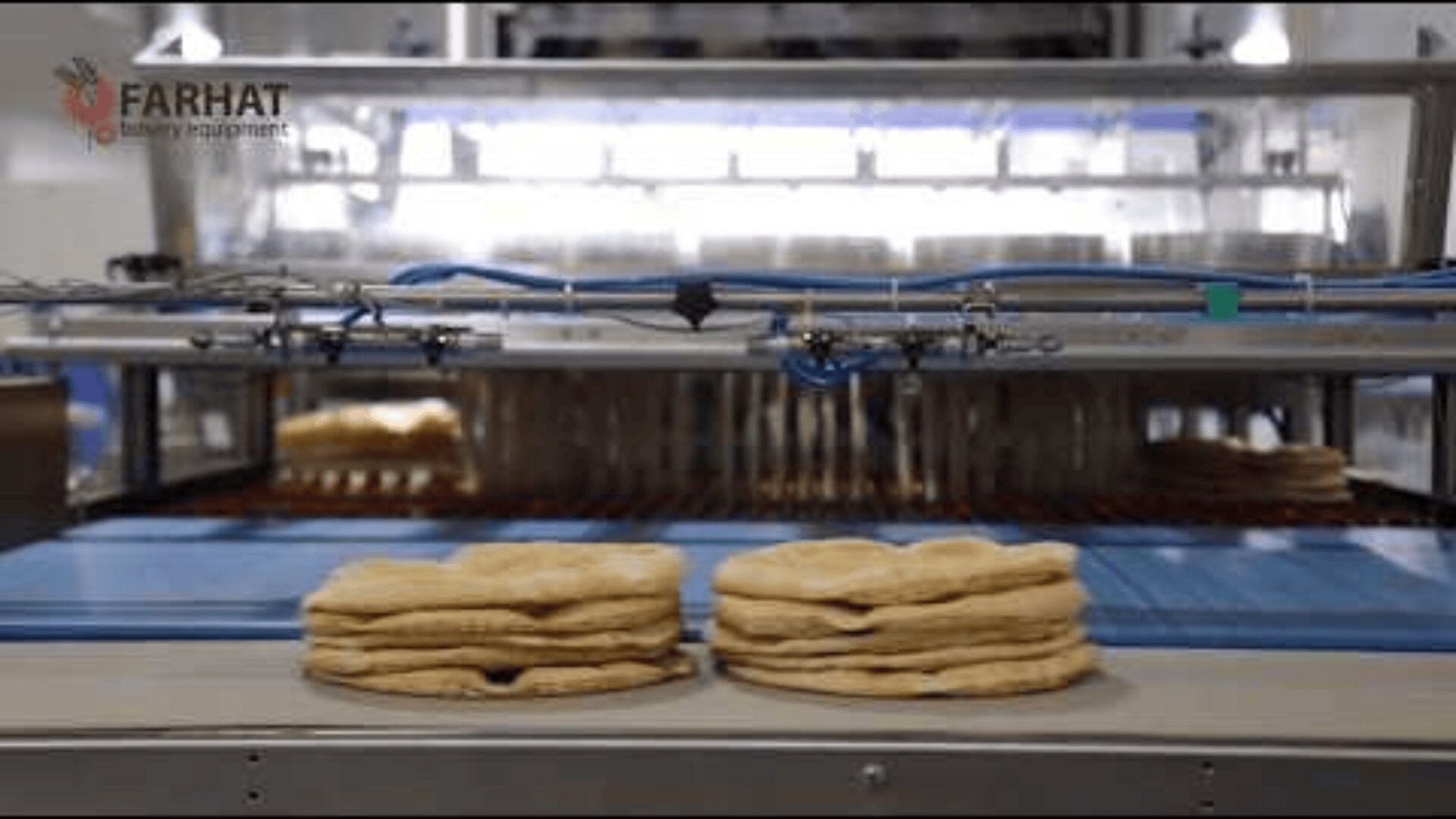 Stacks of flatbread lie on a conveyor belt in front of industrial bakery equipment, with blue cables and metal machinery in the background. The Farhat Bakery Equipment logo appears in the upper left corner.