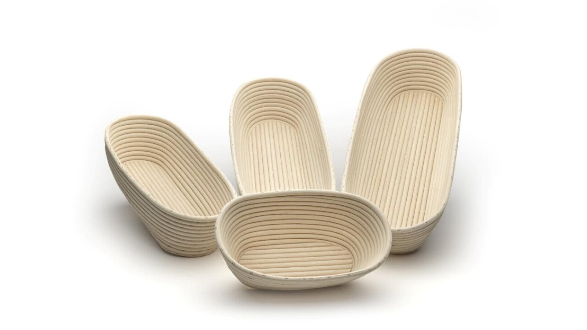Four empty, ribbed banneton bread proofing baskets of different shapes and sizes are arranged on a white background.