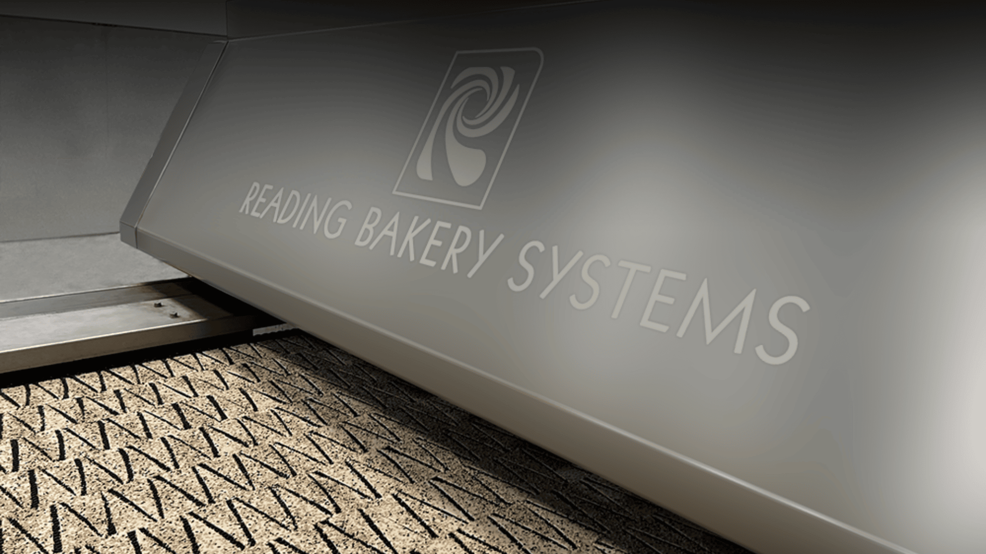 Close-up of a metal machine labeled Reading Bakery Systems above a conveyor belt with evenly spaced rectangular crackers or baked goods.