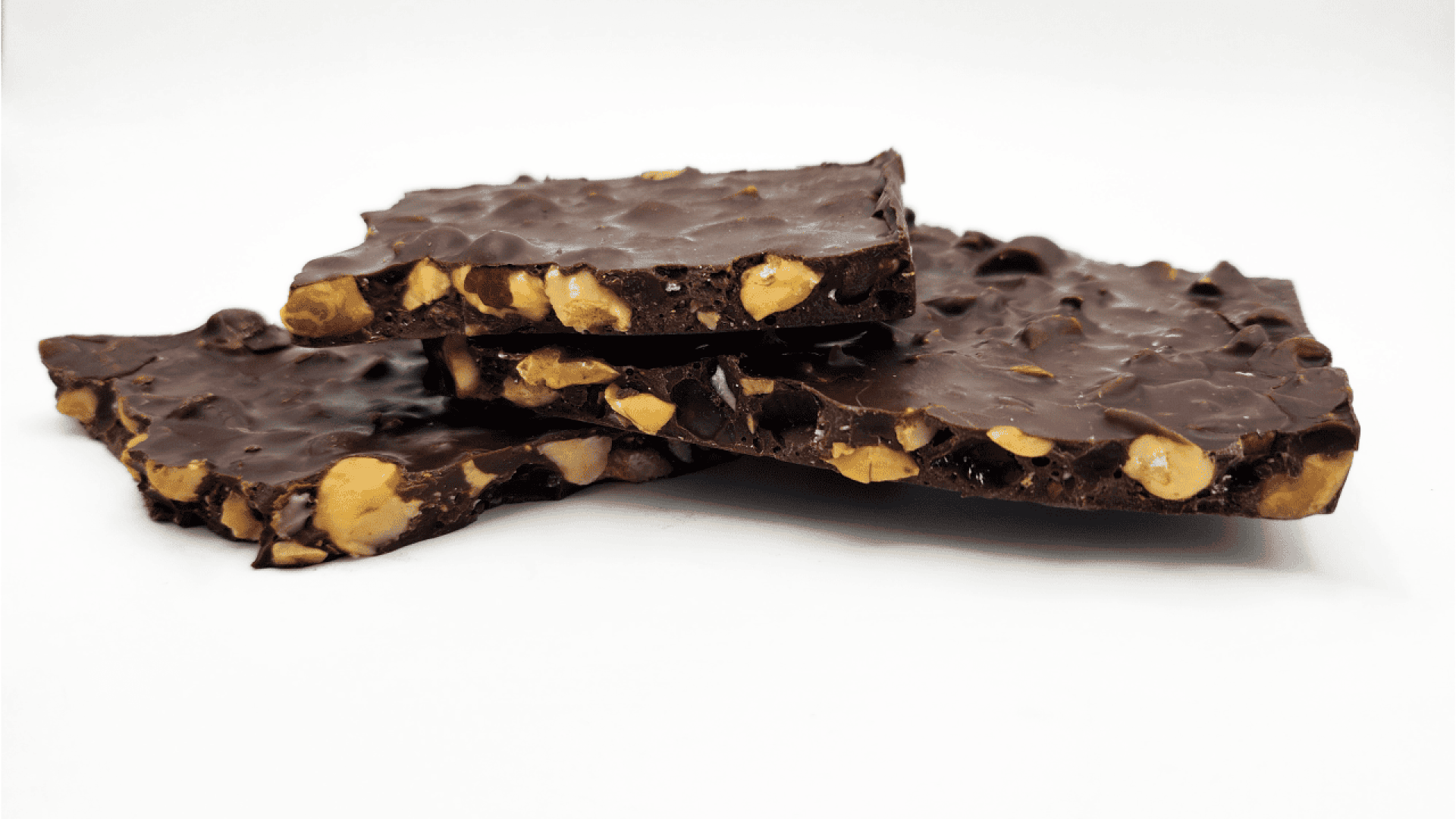 Three pieces of dark chocolate bark with visible whole and chopped nuts stacked on a white background.