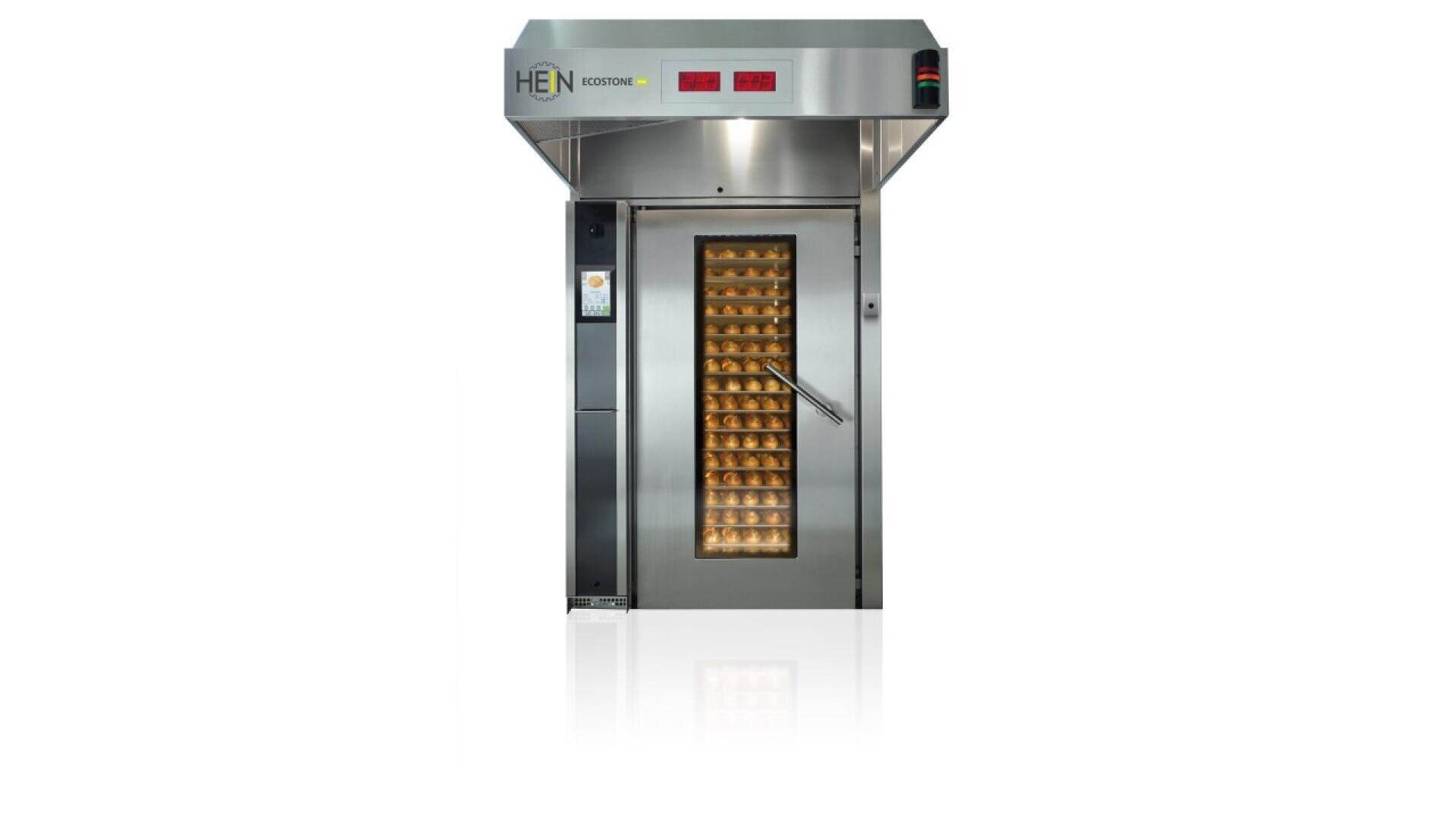 A large industrial stainless steel oven with a glass door displaying multiple trays of baked goods inside. The oven has digital control panels and a vertical touch screen on the left side.