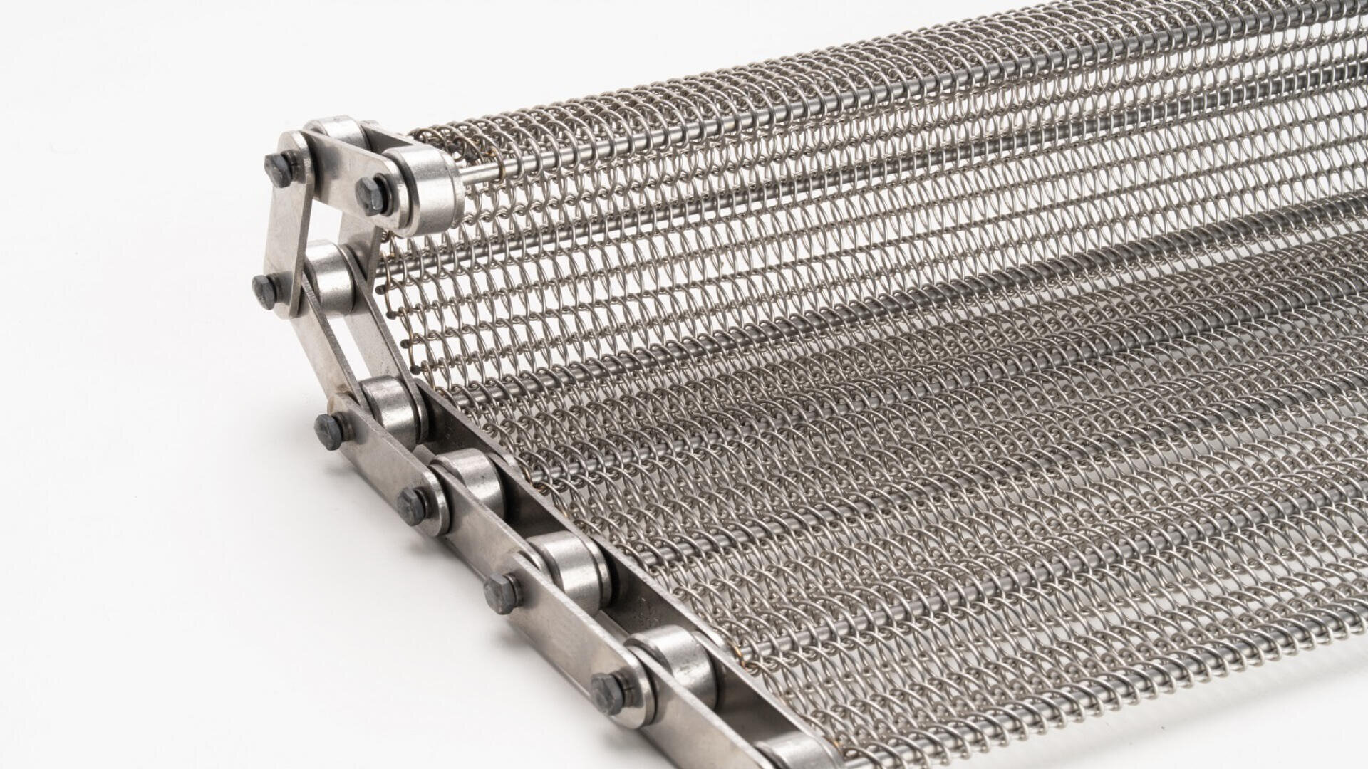 A close-up view of a metal wire conveyor belt with a chain edge, shown against a white background. The belt is made of interwoven, tightly spaced metal wires forming a mesh pattern.