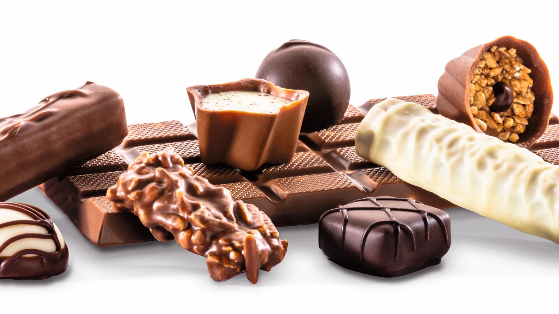 Ein Sortiment von Pralinen, darunter Tafeln, Trüffel und Pralinen aus Vollmilch-, Zartbitter- und weißer Schokolade, angeordnet auf einer Schokoladentafel vor weißem Hintergrund.