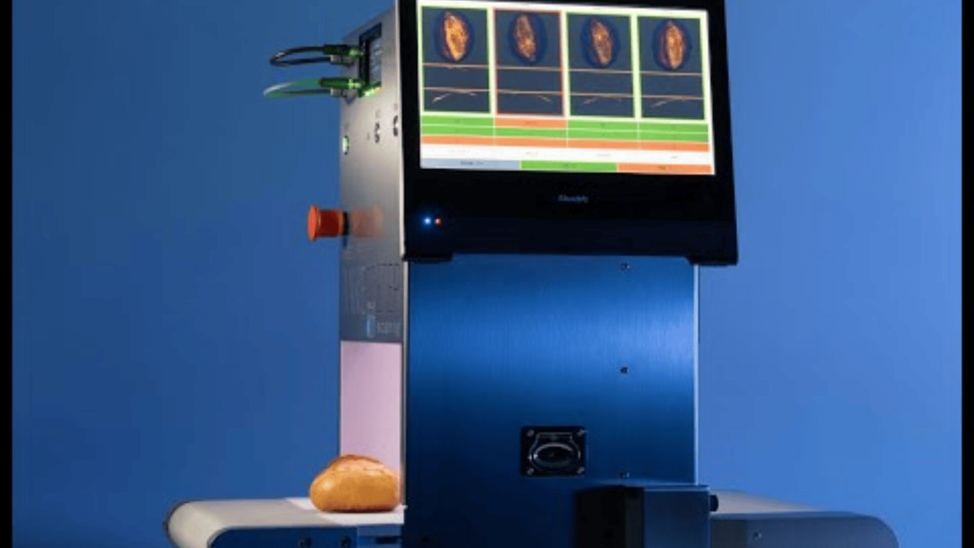 Eine Hightech-Maschine mit einem Bildschirm, der die Scans der Brotanalyse anzeigt, steht auf einem Tisch, durch dessen unteren Teil ein Brötchen vor einem blauen Hintergrund läuft.